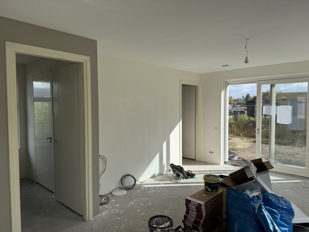 Nieuwe woonkamer tijdens de afwerking, met verfemmers en materiaal op de betonvloer