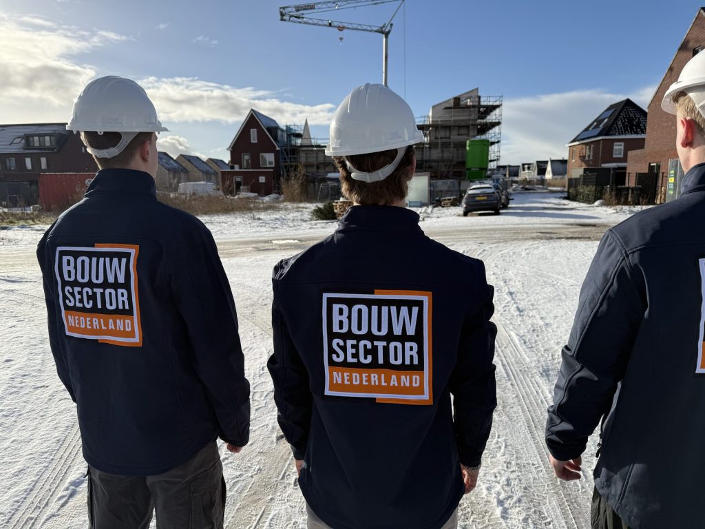 Drie vakmensen van Bouwsector Nederland in bedrijfsjas kijken naar een woning in de steigers